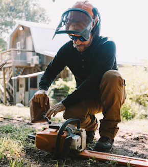 Man refueling a STIHL chainsaw, kneeling and wearing an orange face shield and sunglasses