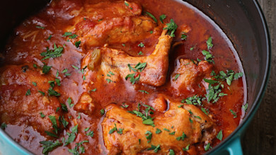 Rabbit cacciatore in blue Dutch oven, rabbit pieces in tomato sauce garnished with parsley