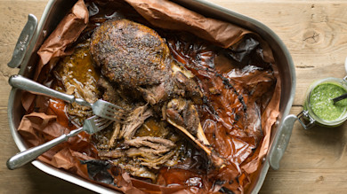 Slow-cooked pork shoulder in roasting pan with two forks shredding and jar of green mojo