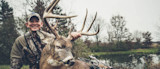 Hunter holding large buck by antlers beside pond, compound bow resting on the deer