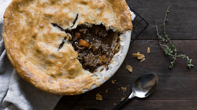 Venison kidney pie with a slice removed revealing stew-like filling, spoon and thyme sprigs