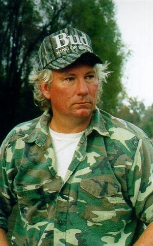 Man in camouflage shirt and cap reading 'Bud King of Beers', outdoors