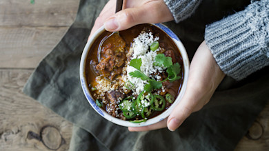 Venison chorizo chili in bowl topped with crumbled cheese, sliced jalapeños and cilantro, hands holding bowl