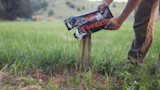 Man pouring granular deer bait from bag labeled "MONSTERMEAL" onto grassy field