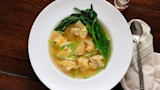 Wontons in clear broth with bok choy and sliced scallions; spoon on cloth napkin