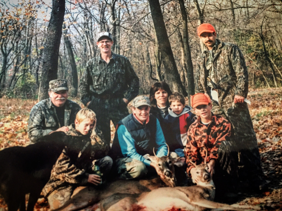Group of adults and children posing with two harvested deer in autumn woods