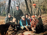 Group of adults and children posing with two harvested deer in autumn woods
