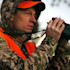 Hunter looking through binoculars wearing orange safety vest and camo hooded jacket