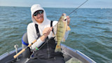 Angler in white hoodie and sunglasses holding a yellow perch aboard a small boat