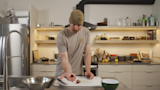 Man in kitchen holding raw gizzard in palm over white cutting board