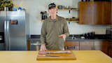 Man removing silverskin from long meat strip on cutting board in kitchen