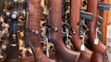Wooden-stock bolt-action rifles with scopes displayed upright, each with a hanging price tag