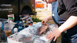 Person in denim apron arranging fish on paint‑splattered table with paint jars; text 'CHRISTIANSHINE 2019' on van
