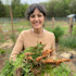 Woman smiling in garden holding freshly pulled carrots with green tops