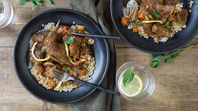 Moroccan-braised rabbit over pearl couscous in black bowls, lemon slices and mint, and a glass of lemon water