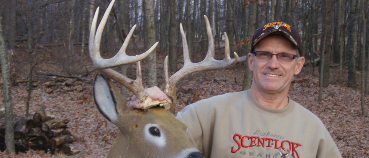 Man in woods holding deer antlers, sweatshirt text 'SCENTLOK'