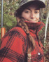 Woman in cap and red plaid jacket with braid, rifle slung on shoulder in forest