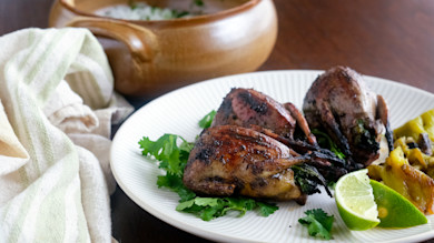 Grilled doves stuffed with hatch chiles on cilantro with lime wedge on white plate