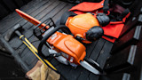 Chainsaw with orange safety helmet and earmuffs, orange vest, sledgehammer and gloves in truck bed
