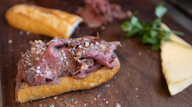 Sliced rare roast beef on toasted baguette with coarse salt, parsley and cheese