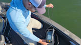 Man kneeling on boat lowering underwater camera into green water