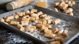 Sweet potato gnocchi pieces dusted with flour on a baking sheet with rolling pin
