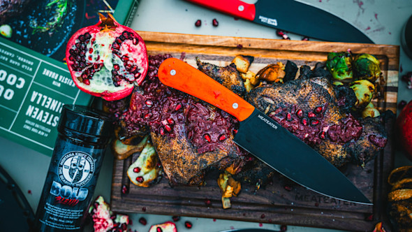 Roast on cutting board with pomegranate seeds and orange-handled knife labeled MEATEATER