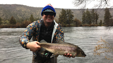 Smiling angler holding large mountain whitefish by river