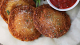 Three crispy fried venison ravioli dusted with grated cheese beside marinara sauce