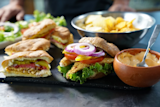 Breaded fish sandwiches with lettuce, tomato, red onion, pickles; bowl of chips and dipping sauce