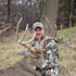Hunter kneeling behind large antlered buck in grassy field by trees