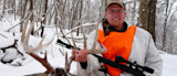 Hunter in snowy woods holding large deer antlers and a rifle, wearing an orange safety vest