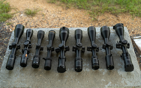 Nine matte-black rifle scopes lined up on a concrete slab