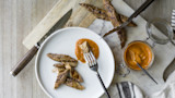 Sliced turkey tenderloin with romesco sauce on white plate, jar of sauce and knife nearby