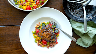 Butter-basted cobia fillet on corn, edamame and tomato salad on plate with fork; skillet with butter and spatula