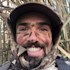 Smiling hunter with black face paint, camo cap and jacket among tall reeds