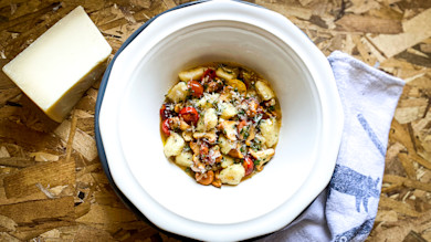 Chanterelle gnocchi in white bowl with cherry tomatoes and grated cheese; cheese block beside