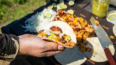 Hand holding tortilla with charred turkey, diced onion, grilled fruit and green sauce