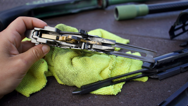 Disassembled shotgun action held over yellow microfiber cloth with cleaning rod nearby