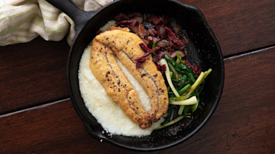 Fried shad roe on creamy grits with sautéed greens and bacon in a cast-iron skillet