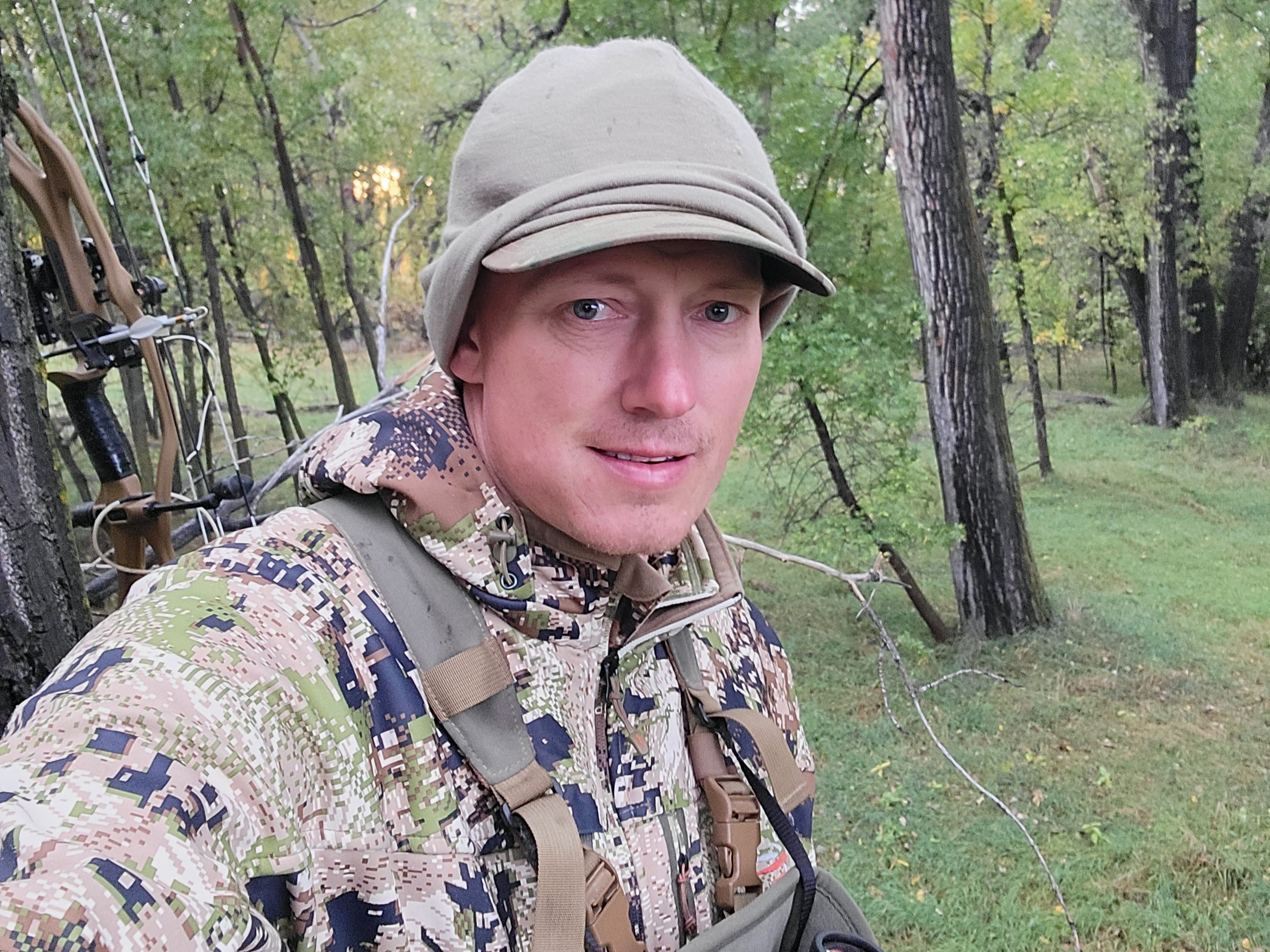 Hunter holding bow in camouflage jacket and hat in a green forest