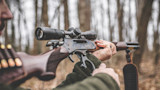 Lever-action rifle with scope being cycled by a hunter in a leafless forest