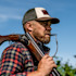 Hunter in plaid shirt carrying an over-under shotgun on his shoulder, whistle in mouth