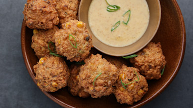 Crispy corn and fish fritters in a brown bowl with creamy dipping sauce and sliced scallions