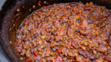 Thick chili with ground meat, kidney and pinto beans simmering in a cast-iron pot