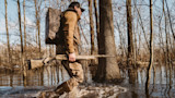 Hunter wading in flooded woods carrying shotgun and blind pack