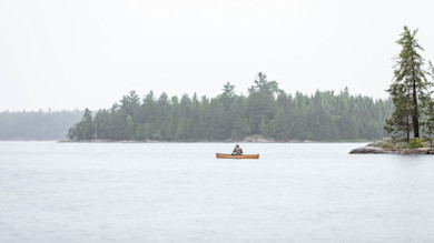 Person alone in canoe on misty lake with tree-lined island behind
