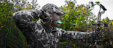 Hunter in camouflage drawing a compound bow in brush, green-fletched arrow at full draw