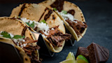 Three shredded mole tacos with cotija, cilantro, lime wedges and chocolate
