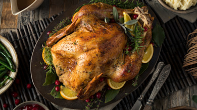 Roasted turkey on platter garnished with orange slices, herbs and cranberries, sides nearby